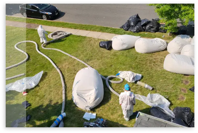 Attic insulation installation with professional equipment and workers on a residential lawn.
